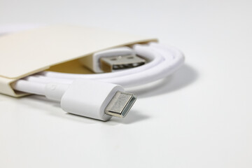 Close up new white USB type charger cable in paper pack, compatible for many devices, wrapped in a spiral shape, isolated on white background.