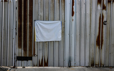 An empty dilapidated cloth notice board on old metal sheet wall near construction site.