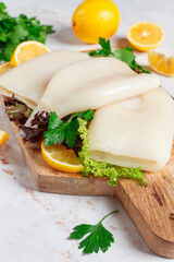 Fresh squid prepared for cooking, surrounded by herbs and lemon, placed on a wooden chopping board in a bright kitchen setting
