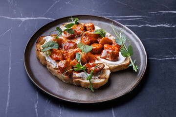 Close-up of tomato bruschetta on artisan bread slices with fresh sliced tomatoes, parmesan cheese and herbs on blue plate, cooking moment. Food preparation process, bruschetta, sandwiches.