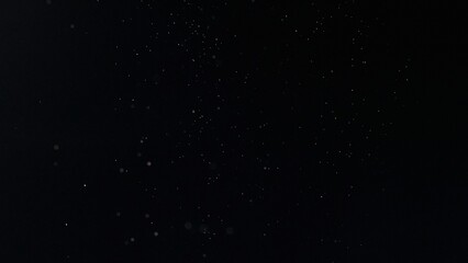 Ethereal white specks drifting in a deep, black void, an atmospheric and minimalist visual depicting dust, snow, or celestial elements for creative projects