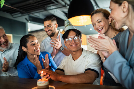 Young adult man celebrating birthday with coworkers at the office, happy