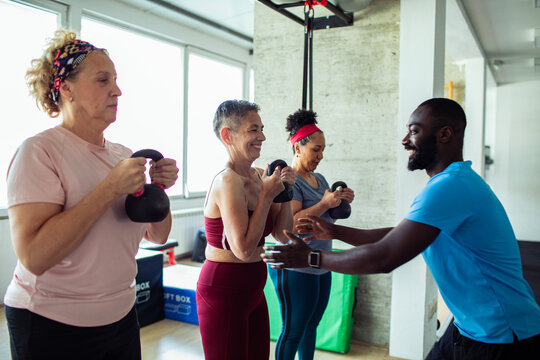 Mature women and adult trainer smiling during kettlebell workout in gym