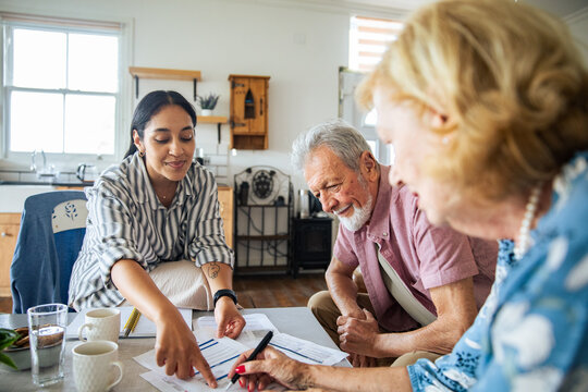 Young advisor guiding smiling senior couple with paperwork at home