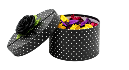 A decorative black polka dot round gift box overflowing with colorful flower petals isolated on transparent background