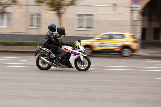 Two people are riding a motorcycle through a summer city