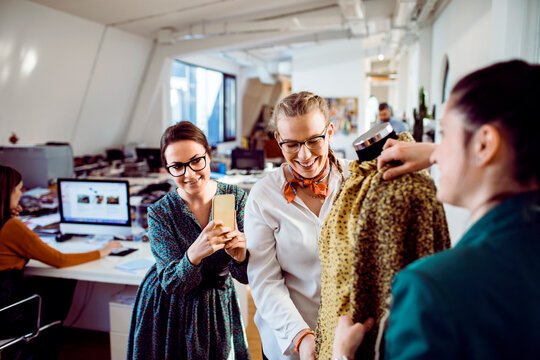 Young adult women smiling while styling dress on mannequin in modern fashion studio