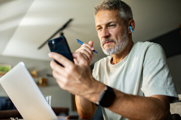 Mature man concentrating on smartphone while working from home
