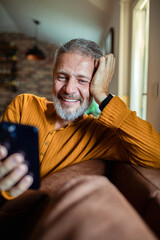 Mature man smiling at smartphone at home