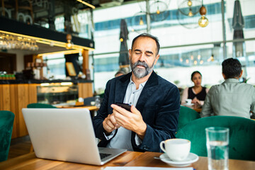 Mature man focused on smartphone while working at cafe