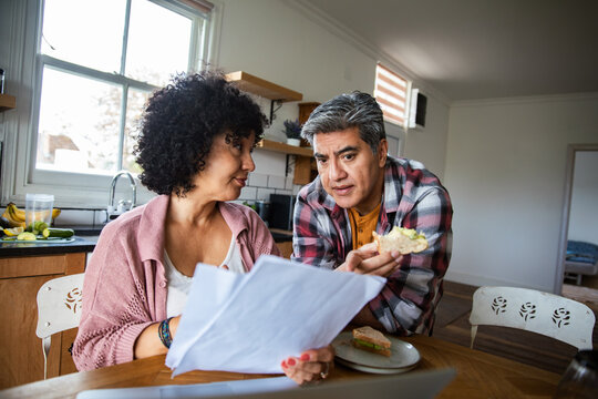 Adult couple reviewing bills with concerned expressions at home kitchen