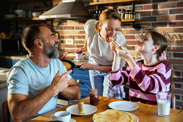 Joyful adult parents with child daughter making pancakes in home kitchen