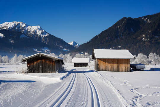 Cross-country skiing trail between wooden mountain sheds on beautiful sunny day, Ehrwald, Zugspitze Area, Austria - Powered by Adobe