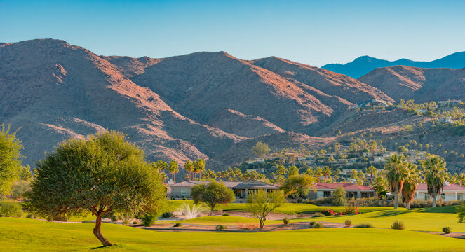 Houses climb the mountain side in front of  a green belt in Palm Springs, California
