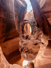Narrow sandstone passage with sculpted walls and a natural arch in Peekaboo Canyon