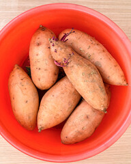 Top view of sweet potatoes in red plastic basin.
