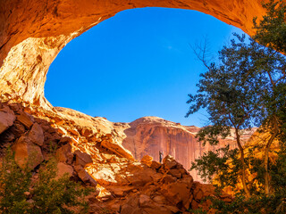 Sunlit Jacob Hamblin Arch framing a rocky canyon with a tiny hiker