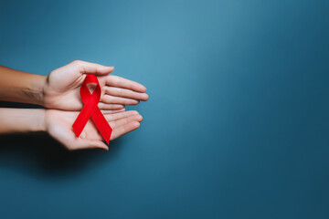 Ruban rouge symbole du Sidaction tenu dans deux mains ouvertes sur fond bleu avec espace négatif copyspace visuel de sensibilisation lutte contre le sida Journée mondiale 1er décembre