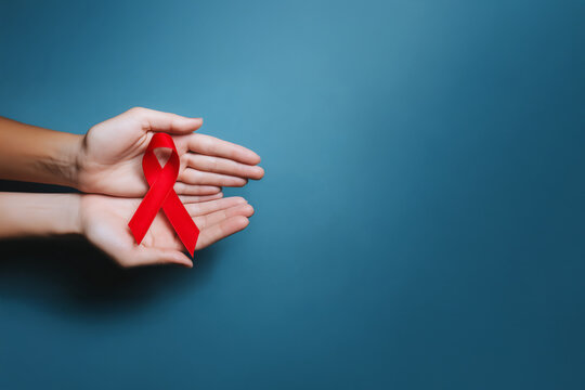 Ruban rouge symbole du Sidaction tenu dans deux mains ouvertes sur fond bleu avec espace n&eacute;gatif copyspace visuel de sensibilisation lutte contre le sida Journ&eacute;e mondiale 1er d&eacute;cembre