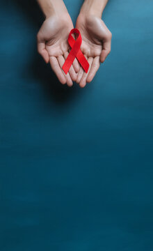 Ruban rouge symbole du Sidaction tenu dans deux mains ouvertes sur fond bleu avec espace n&eacute;gatif copyspace visuel de sensibilisation lutte contre le sida Journ&eacute;e mondiale 1er d&eacute;cembre
