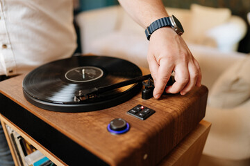 Hand lowering tonearm on vinyl record player, cozy home audio setup