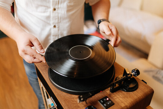 Placing a vinyl record on a wooden turntable at home, cozy audiophile moment