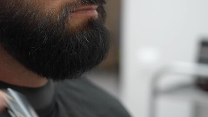 Man's beard is carefully combed, trimmed and shaped at a modern barbershop. The barber skillfully uses scissors and a comb to create an elegant look straight view