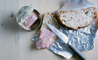 A piece of bread with a knife on it and a can of food next to it. Scene is casual and relaxed