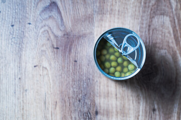 A top table view of can of green beans open on a wooden table. The beans are in a liquid, and the can is partially empty