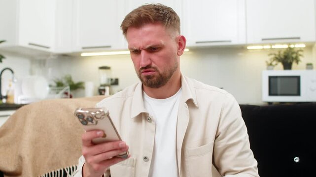 Young man at home uses glasses and checks smartphone reads small text and tests focus with calm breath. Caucasian guy on sofa sees surprising news in messenger and shows clear vision with mild shock.