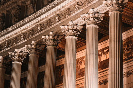 Close-up night shot of a row of illuminated Corinthian columns and the decorated entablature of a grand historic building.