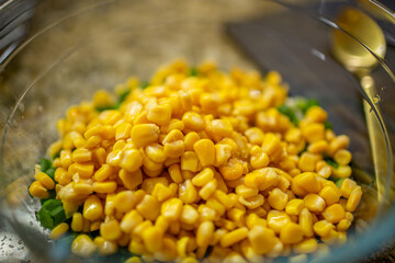 Vibrant yellow corn kernels piled on top of chopped green onions in a clear glass bowl on a brown granite kitchen countertop