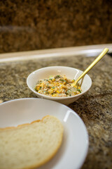 Close-up of a golden spoon lifting a mixture of tuna, corn, and eggs from a glass bowl while preparing a healthy homemade salad