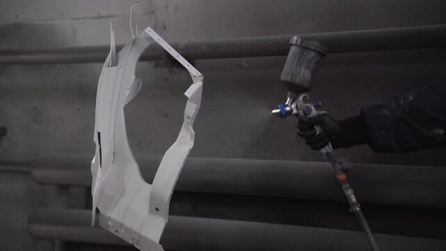 A car painter paints a part in a paint booth using a spray gun.
