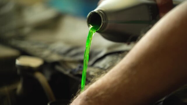 A car mechanic pours green antifreeze at a service center.