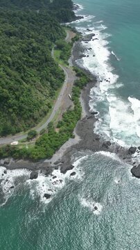Vertical aerial view of the coastline full of vegetation and turquoise sea with reefs near the Jacó Beach viewpoint located in the province of Puntarenas in Costa Rica