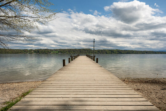 A small wooden dock stretches into a peaceful lake, used for small boats, fishing, or quiet relaxation. Serene water, natural surroundings and soft light create a tranquil outdoor scene.