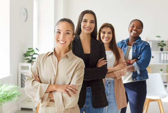 Portrait of confident female business people looking cheerful at camera and smiling standing in a row with crossed arms indoors. Women company employees group standing in office confidently.