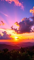 A vibrant sunset over mountain ranges with dramatic clouds and colorful sun rays