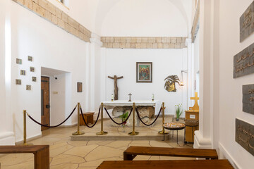 HAIFA, ISRAEL, June 26, 2025: Muhraka monastery of the Carmelite on the Carmel mount. interior of a small chapel with a simple stone altar, wooden cross, and religious artwork on the white walls
