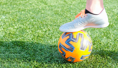 Football players foot in cleats resting on a soccer ball on green grass. Close-up sports moment symbolizing training, teamwork, competition and active lifestyle.
