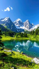 Fototapeta premium Snowy peaks reflect in a clear alpine lake amid green hills under a blue sky