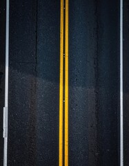 An overhead shot of a wet asphalt road with double yellow lines