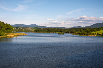 A stunning lake landscape framed by forest trees and distant mountains. Calm water, natural colors, and peaceful scenery create a perfect outdoor nature view.