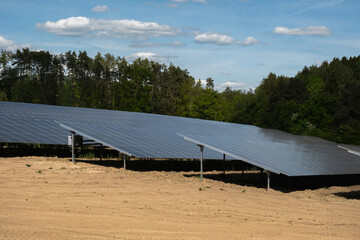 Rows of solar panels cover a field with mountains and forest in the background. Clean energy concept in a natural landscape with sunlight and sustainable technology.