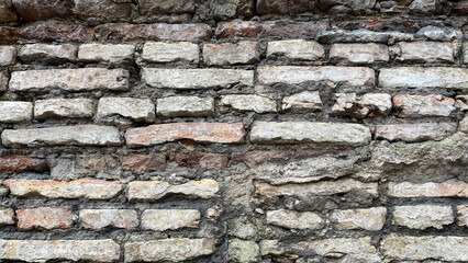 Close-up of an old brick wall with uneven layers, weathered mortar, and rough texture, showing rustic and historical construction details.