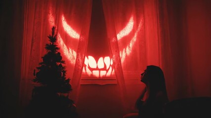 Woman interacts with glowing evil face projection on curtain next to Christmas tree, Halloween fear concept. - Powered by Adobe