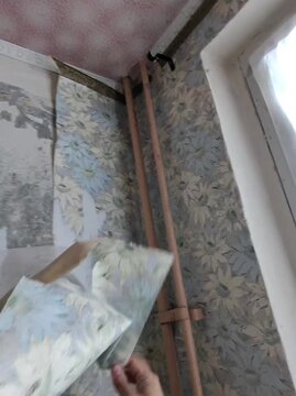 A man removes wallpaper with a putty knife. First-person view. A first-person view of the process of removing old wallpaper from walls. Vertical video.