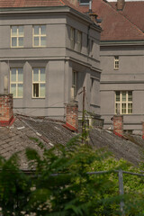 grey rooftop with chimneys and windows overlooking leafy foreground, weathered terracotta tiles, brick