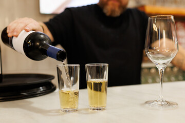 Bartender's hand pouring white wine from a bottle into a small glass on a bar counter